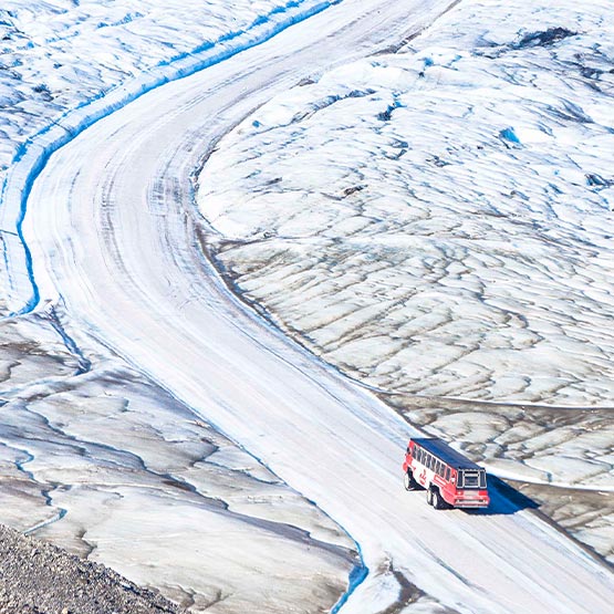 A large Ice Explorer bus drives on a glacial ice road.
