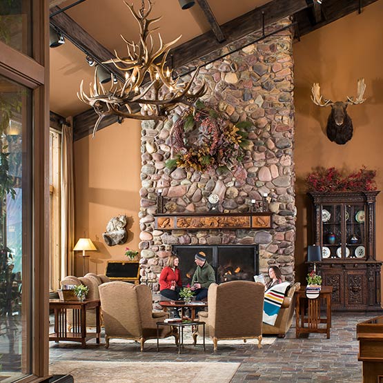 Guests sit in the hotel lounge with a large stone fireplace behind them.