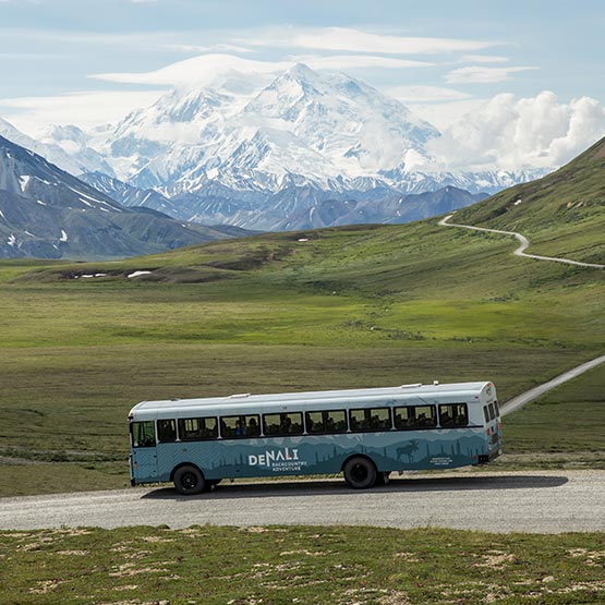 A tour bus stopped on a gravel road in a wide mountain valley.